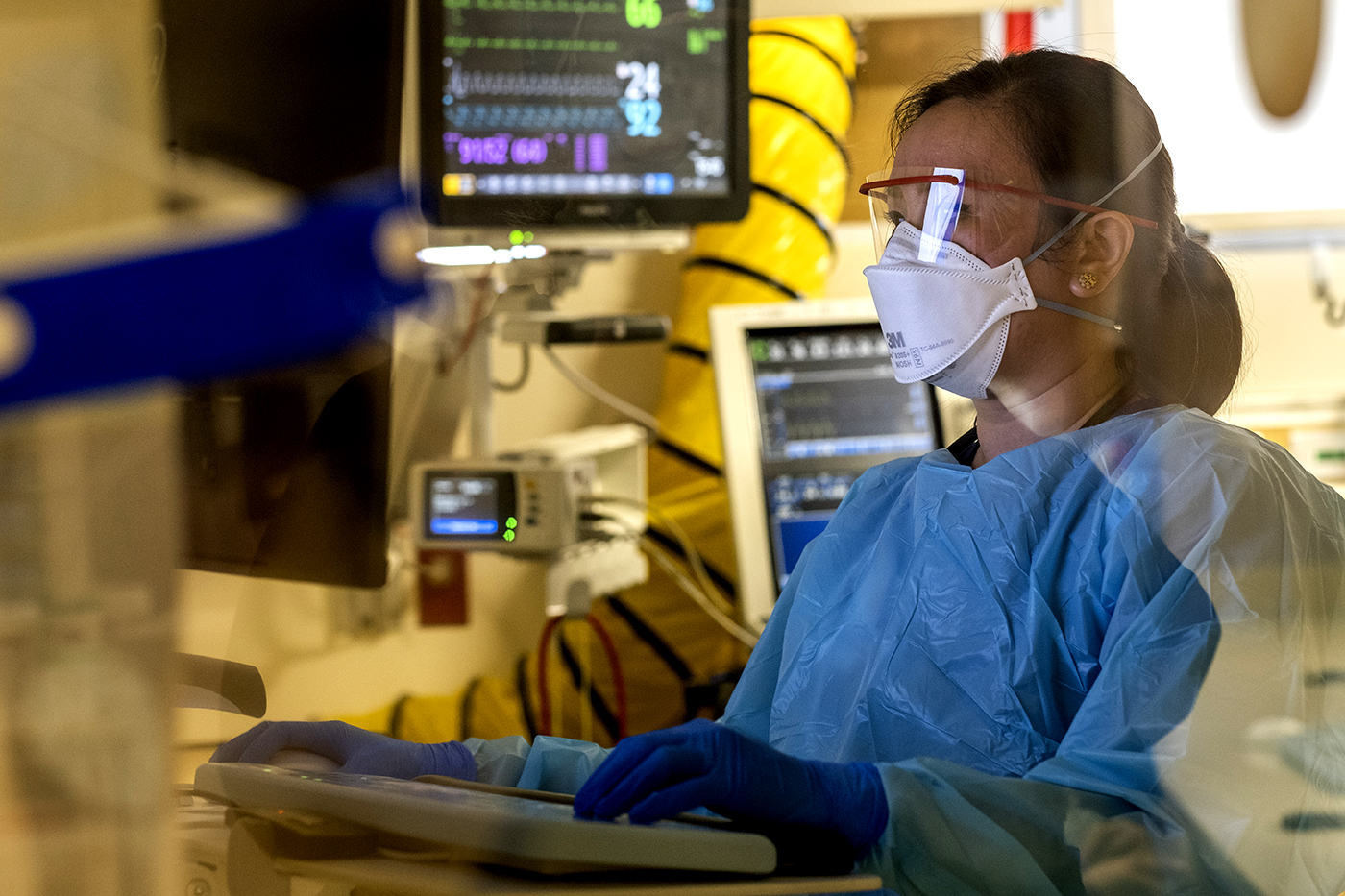 Woman in protective medical gear at a computer in an intensive care setting